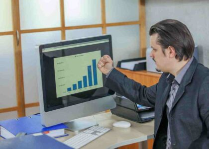 Businessman celebrating as bar chart on monitor shows growth from cost estimation techniques.